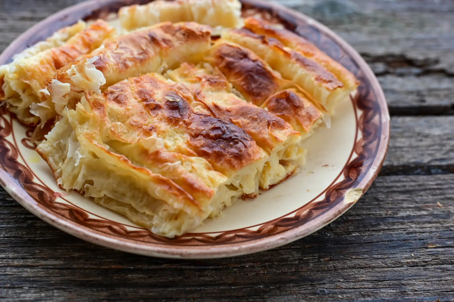 Zapečena pita na ukrasnom tanjiru na drvenom stolu
