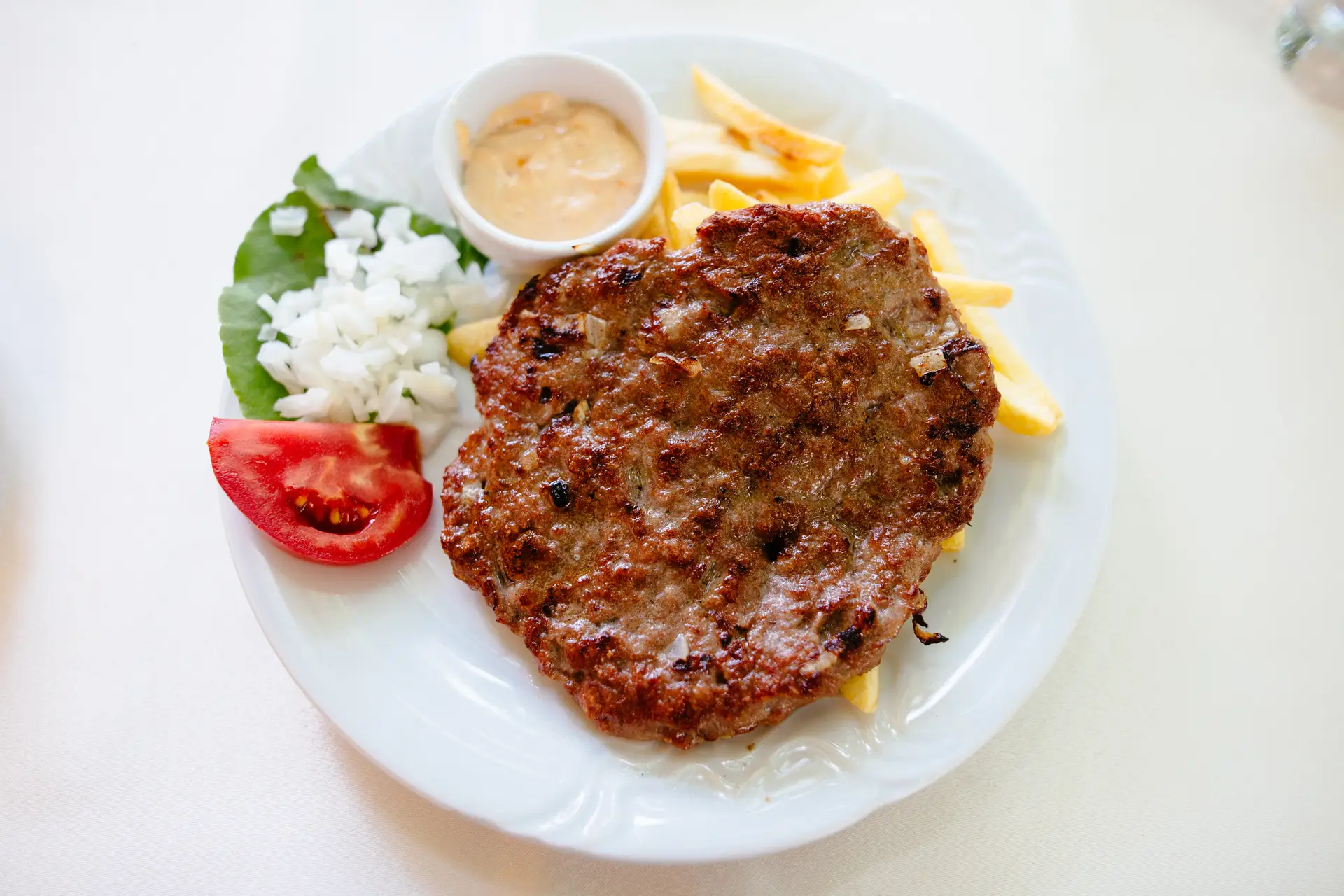Pljeskavica sa pomfritom, lukom, paradajzom i sosom na tanjiru