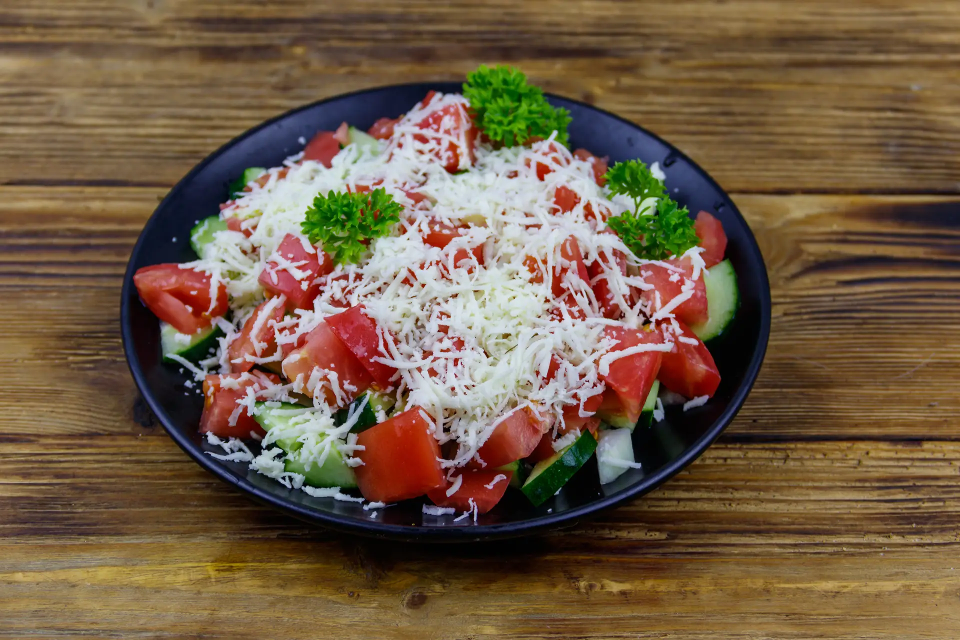 Šopska salata na crnom tanjiru, sa sirom i peršunom