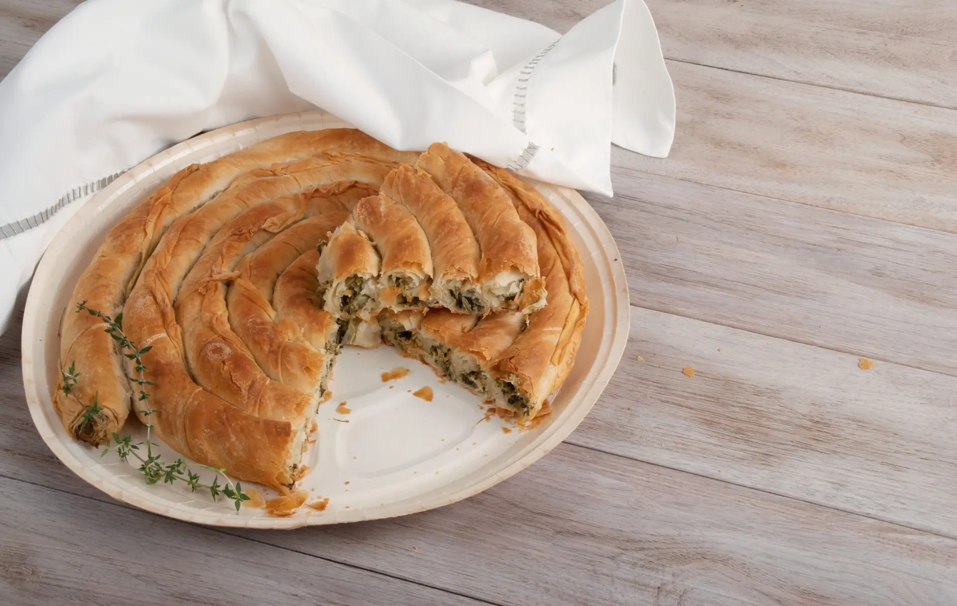 Okrugli burek na tanjiru, isečen komad, grančice timijana